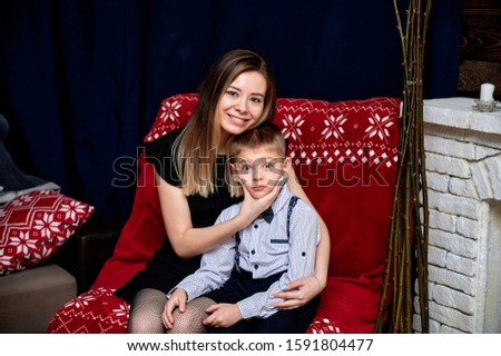 Portrait of a happy family: mom and a cute boy 10 years old schoolboy at home on the sofa in a loft style. Sitting right in front of the camera, showing emotions, smile