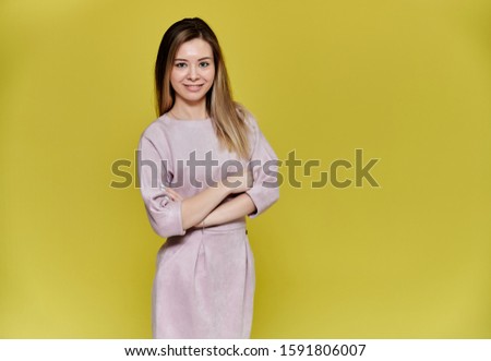 Portrait of a pretty young smiling woman on a yellow background in a pink dress with long straight hair. Standing right in front of the camera, Shows emotions, talks in different poses.