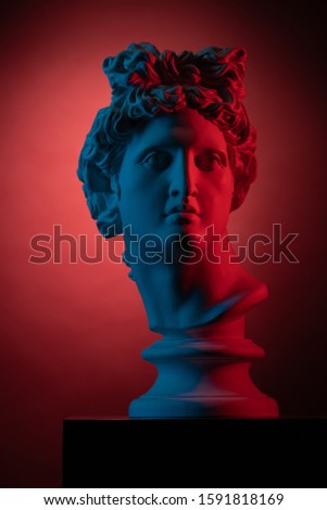 Plaster statue bust of Apollo Belvedere in red and blue light on a red background