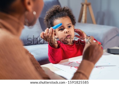 Happy African American mother assisting her daughter in coloring.