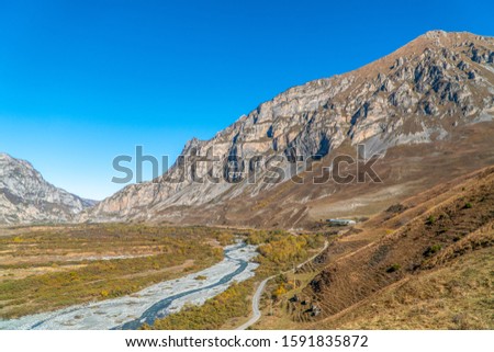 North Ossetia. Mountain peaks in the fall. Orange tree crowns. Falling foliage. Sunny clear weather