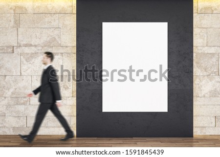 Businessman walking in gallery interior with empty billboard on wall. Mock up,