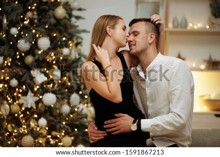couple in love kisses and hugs on the sofa near the Christmas tree lights. New year's night.Christmas. black dress and white shirt, jewelry
