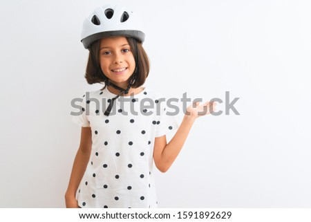Beautiful child girl wearing security bike helmet standing over isolated white background smiling cheerful presenting and pointing with palm of hand looking at the camera.