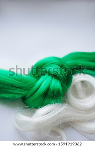 a strand of white and green artificial hair on a gray background