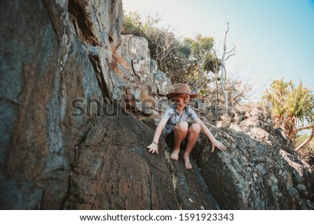 Young boy wearing cowboy hat exploring rocks on the beach at Conway Beach in Queensland, Australia
