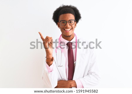 Young african american doctor man wearing pink stethoscope over isolated white background with a big smile on face, pointing with hand and finger to the side looking at the camera.
