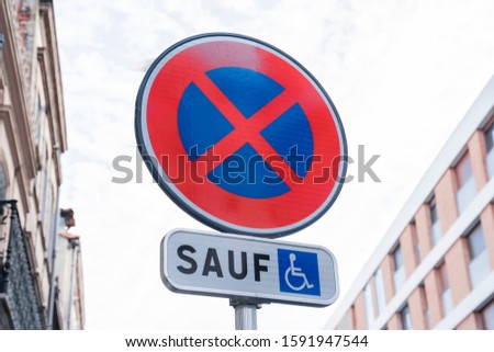 Road sign prohibition of stopping transport, with a white sign and with the inscription in French "except for the disabled" against the background of the apartments of the sleeping area of ​​the city.