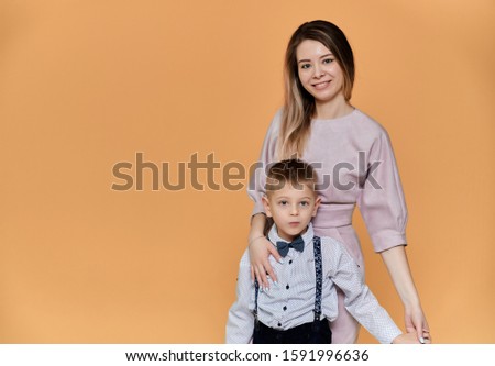 Portrait of a happy family: mom and a cute boy of 10 years of schoolboy on a beige background in trousers and a shirt. Standing right in front of the camera, showing emotions, smile
