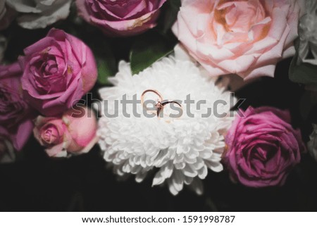 Picture of two rings sitting in a white flower which is part of a Bouquet of roses