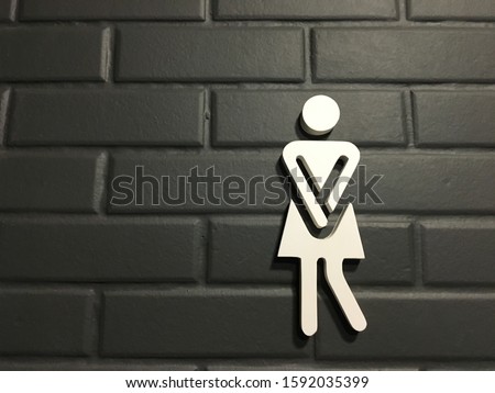 Urinary Urgency Toilet Sign for women at the entrance to a public toilet. Comic toilet sign symbols with woman on black brick background. Copy space. Royalty-Free Stock Photo #1592035399