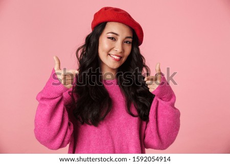 Image of young beautiful asian girl wearing beret smiling and pointing fingers at you isolated over pink background