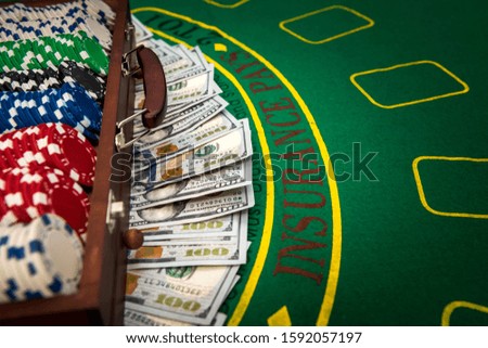Gambling concept. Colorful poker chips with american dollars in wooden box on green playing table.
