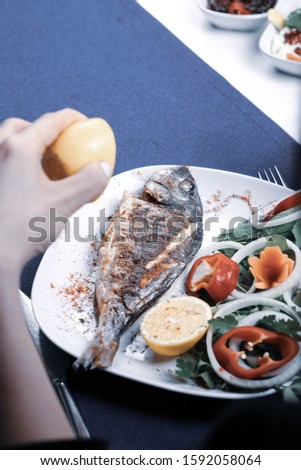 Fried sea bream (cupra) fish on white plate with onion, garden rocket and lemon slices