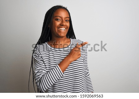 Young african american woman wearing striped t-shirt standing over isolated white background cheerful with a smile of face pointing with hand and finger up to the side happy and natural