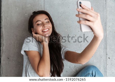 Attractive smiling young brunette woman wearing casual clothes sitting on a couch, taking a selfie