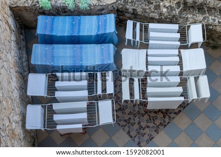 Looking down on an open air patio with seven metal clothes driers (horses) draped with blue and white sheets, towels and bedding. Using the renewable energy of air and sun to dry the laundry.