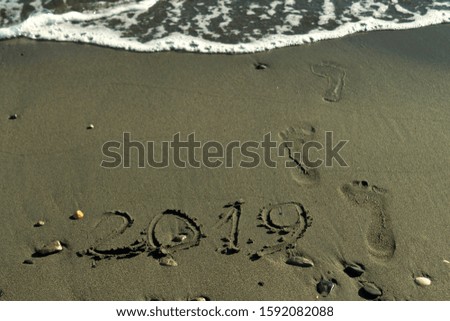 Number 2019 written on the wet sand at the beach, footprints and a wave is about to erase everything