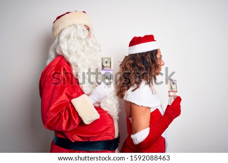 Senior couple wearing Santa Claus costume holding dollars over isolated white background looking to side, relax profile pose with natural face and confident smile.