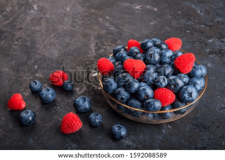 Fresh blueberries and strawberries in a glass bowl and on a dark background, top view