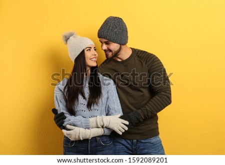 Happy young couple in warm clothes on yellow background. Winter vacation