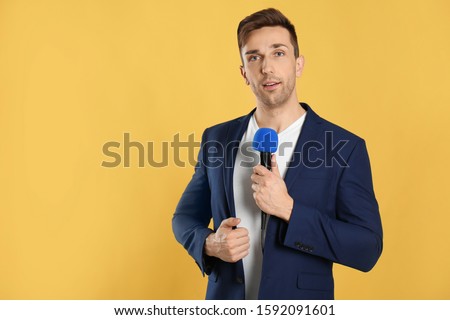 Young male journalist with microphone on yellow background. Space for text