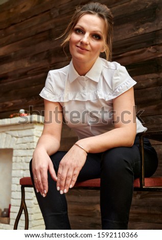 Portrait of an adult pretty woman 40 years old with good makeup on a background of wood. Sits on a stand right in front of the camera with a smile. Business concept.