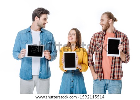 smiling three young friends holding digital tablets with blank screens isolated on white