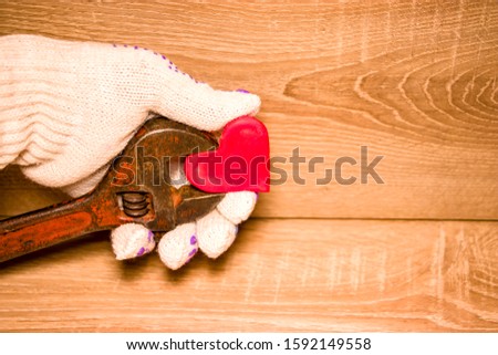 Valentine's Day. Red heart in male hands in gloves held by an adjustable wrench. On a wooden background. Concept for design.