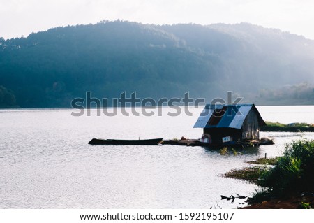 Landscape photo of Tuyen Lam lake of Da Lat on a sunny afternoon with mountains and forest on the other side of the lake. There are a small fisherman's hut floating near the lake bank