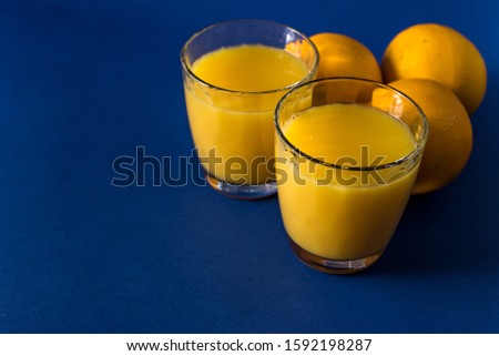 glass of fresh juice and orange on a classic trendy blue background with striped straws