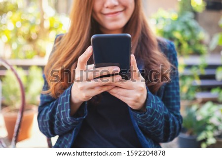 Closeup image of a beautiful asian woman holding , using and looking at mobile phone in the outdoors