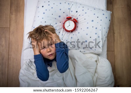 Top view. Crazy tired child boy sleep in bed with alarm clock. Time to get up.  Royalty-Free Stock Photo #1592206267