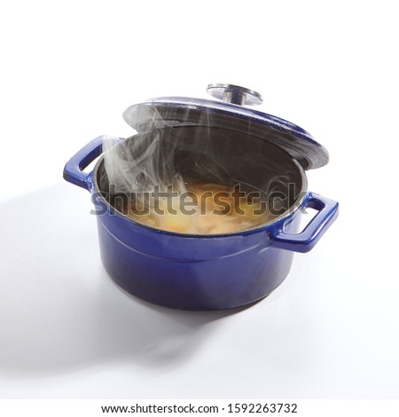 Homemade chicken soup with potatoes, carrots and onions in a blue pan isolated on white background side view. Traditional meat seasoned broth, sturdy clear bouillon in cook pot closeup