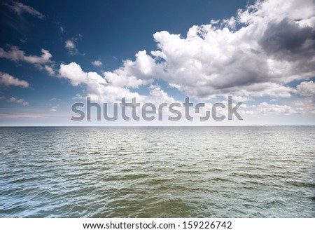 White fluffy clouds blue sky above a surface of the sea