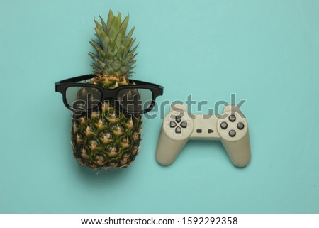 Gamer concept. Fun and humor. Pineapple in sunglasses and gamepad on blue background. Top view
