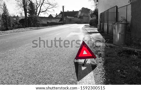 Red warning triangle. Road sign on black and white village background. Attention! Danger on the way. Caution symbol on asphalt surface. Idea of traffic regulations, rules, safe travel or car accident.
