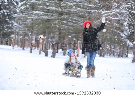 Winter fairy tale in the forest. A girl on a sled with gifts on the eve of the new year in the park. Two sisters walk in a New Year's park and ride a sled with gifts.
