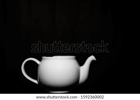 Photo of a white ceramic kettle with shadows from light and a black background.