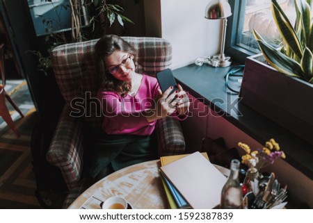 Adult girl in glasses takes a selfie while sitting in a cafe at her leisure