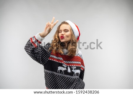 A girl of European appearance demonstrates emotions. She wears a blue sweater on which deer are painted. Isolate on a white background. Beautiful young blonde. Santclaus hat.