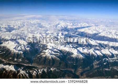 Winter landscape. Beautiful Alps mountains with peaks covered in snow. Photo from the porthole of an airplane.