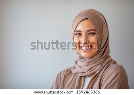 Woman in traditional Muslim clothing, smiling. Beautiful woman headshot looking at camera and wearing a hijab. Arabian woman with happy smile. Strict formal outfit and elegant appearance. Islamic Royalty-Free Stock Photo #1592465386