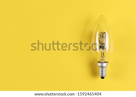 Close up studio photo of burned-out halogen bulb with E14 base on yellow background. Light bulb symbol of ideas. Recycling of incandescent halogen lamp. Royalty-Free Stock Photo #1592465404