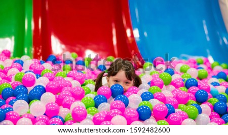 happy little preschooler girl with ponytails in a white t-shirt plays in the pool with colorful balloons on the playground. banner.