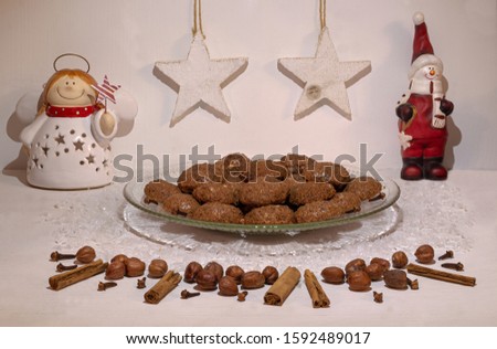 festive scenery showing homemade christmas chocolate cookies on a glass plate; front view with decorative ornaments, spices and hazelnuts on white wooden table