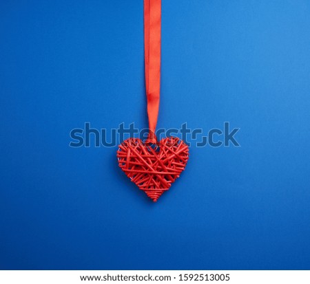red wicker decorative heart hanging on silk ribbon, blue festive background for Valentine's day