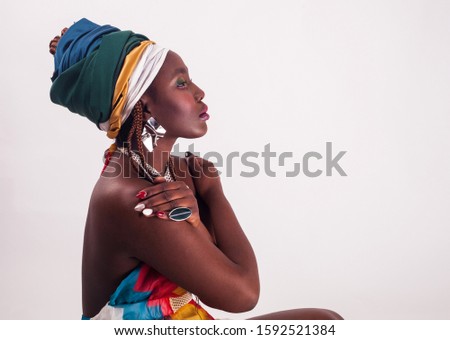 Studio fashion portrait of young African ethnicity woman in summer colorful dress and ethnic head wrap, white background.