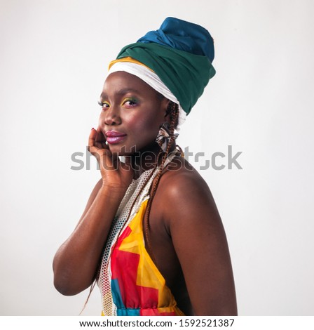 Studio fashion portrait of young African ethnicity woman in summer colorful dress and ethnic head wrap, white background.