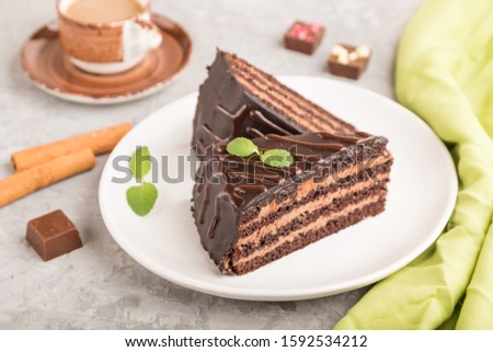 Homemade chocolate cake with milk cream and a cup of coffee on a gray concrete background with green textile. side view, close up, selective focus.